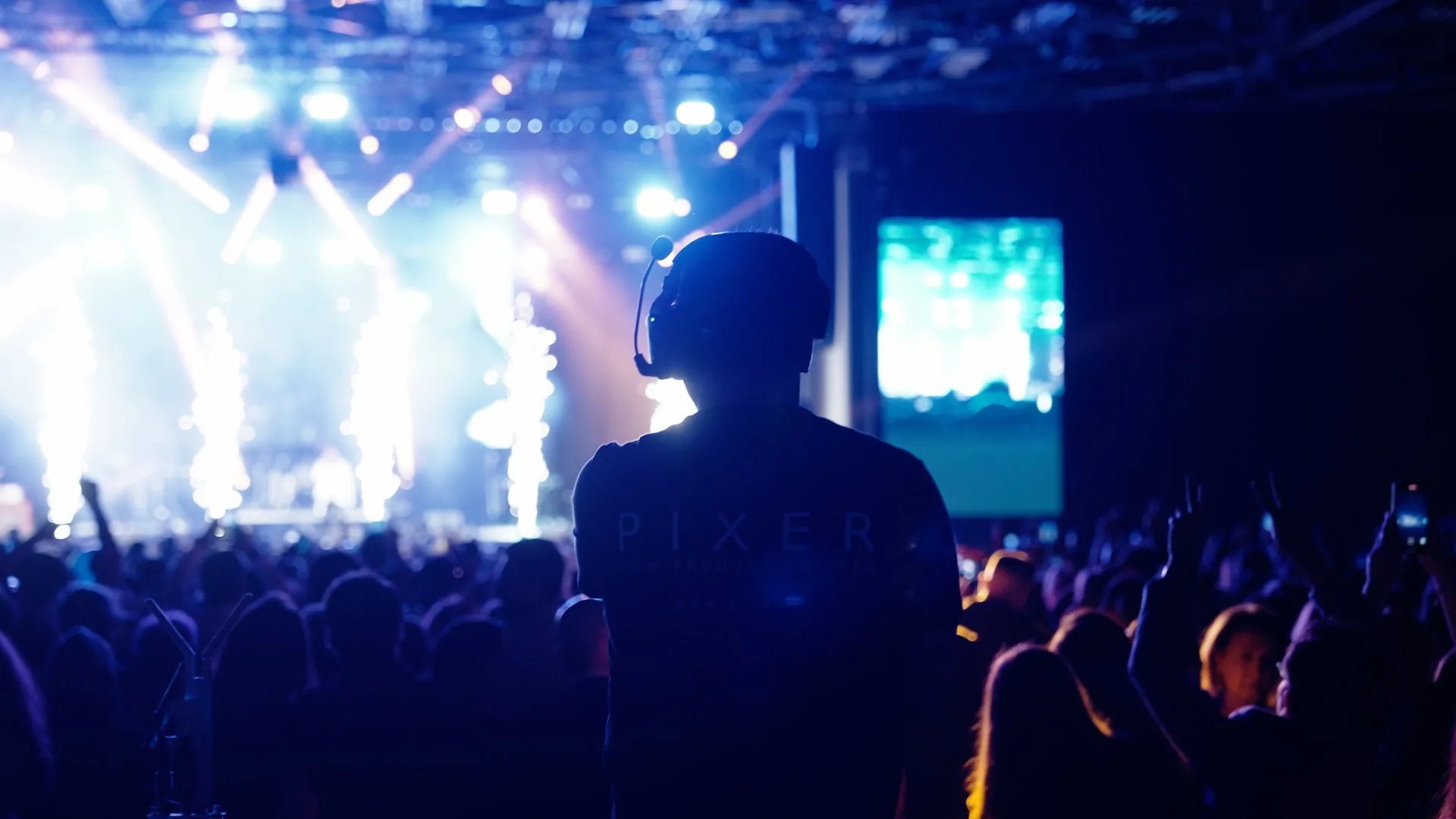 Silhouette eines Pixer-Teammitglieds vor einer vollen Konzertbühne mit dramatischem blau-weißem Licht